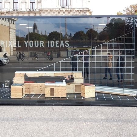Ein Container mit Glasfassade und einer Person die im Inneren auf einer Holzbank liegt