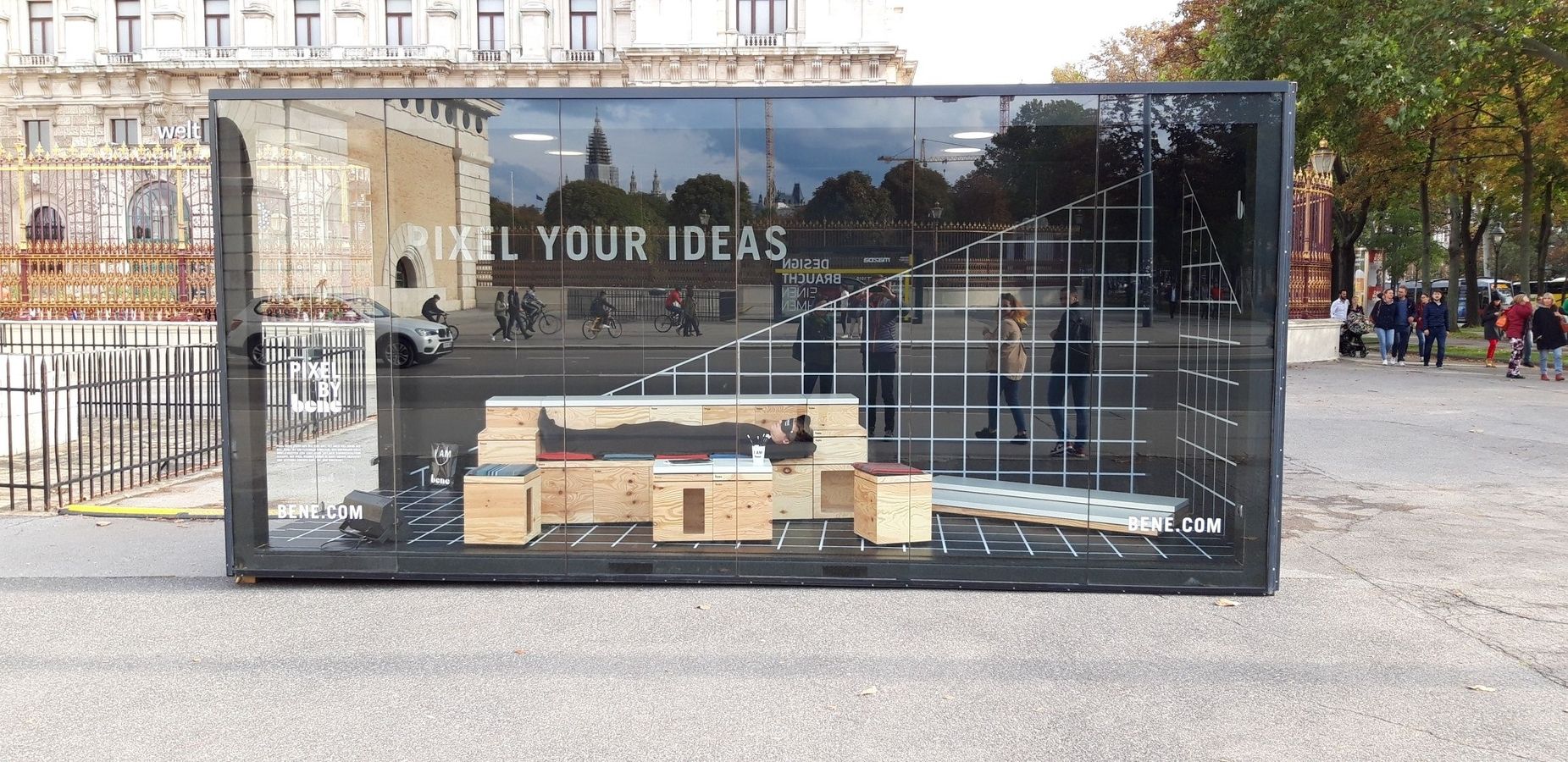 Ein Container mit Glasfassade und einer Person die im Inneren auf einer Holzbank liegt