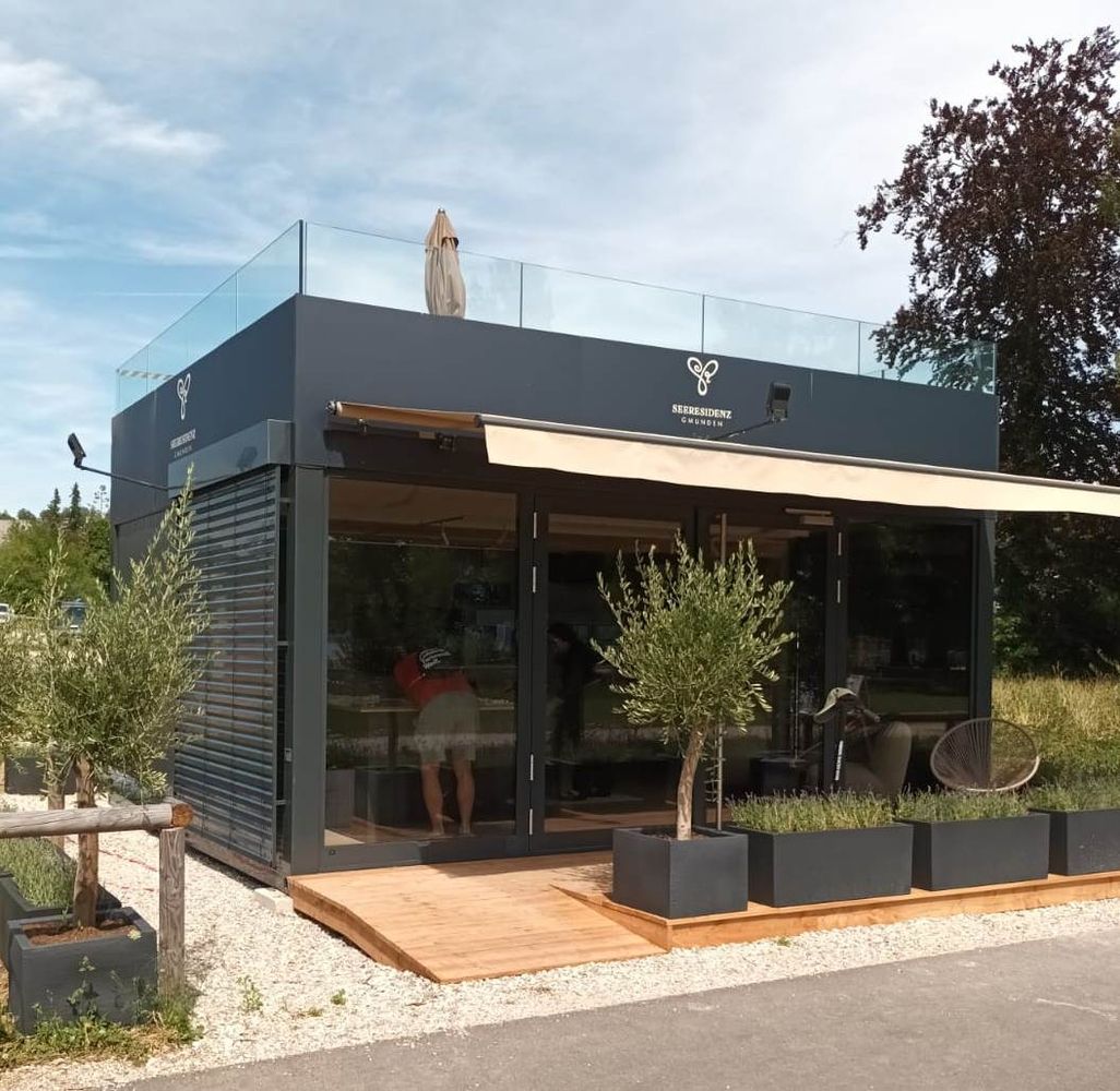 Ein schwarzer Container mit Markise und Dachterrasse