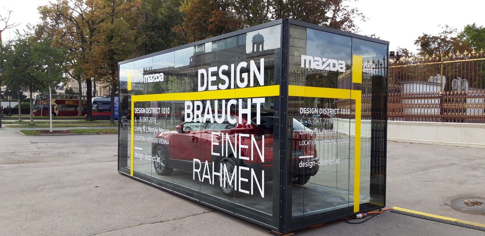 Ein Promotioncontainer mit Glaswänden und einem roten Mazda im Inneren